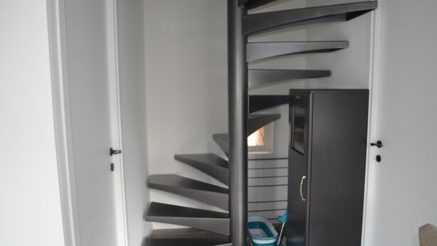 A spiral staircase with a dark-colored handrail and steps, leading to a door with a handle. - Country cottage (Raon-aux-Bois)