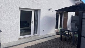 A white house with a sliding glass door, a patio with a table and chairs, and a black umbrella. - Country cottage (Raon-aux-Bois)