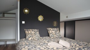 A bedroom with a bed, two patterned pillows, and three wall-mounted sunburst decorations. - Country cottage (Raon-aux-Bois)