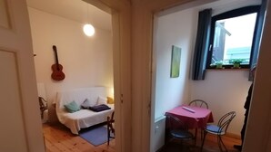Een gezellige kamer met een witte bank, een gitaar en een zithoek met een tafel en stoelen.