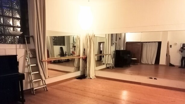 Een kamer met een grote spiegel, houten vloer en een piano.
