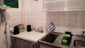 Een moderne keuken met witte tegels, een zwart inductiekookveld, een spoelbak en een schilderij van een groen landschap aan de muur.