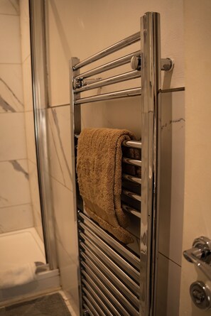 A bathroom with a glass shower door, a towel rack with a towel, and a metallic towel warmer. - Brighton High Road Beach Studio (Brighton and Hove)