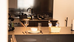 A modern kitchen with a dining area, including stools, a wine glass, and a basket with water bottles. - Brighton High Road Beach Studio (Brighton and Hove)