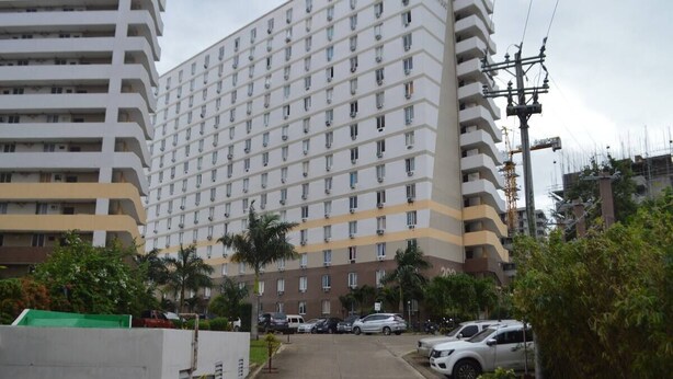 A multi-story hotel with a uniform facade, a parking area with cars, and a clear sky.