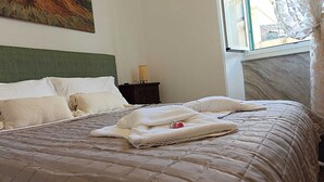 Una cama bien hecha con colcha acolchada y varias almohadas, una lámpara de noche y un cuadro en la pared.