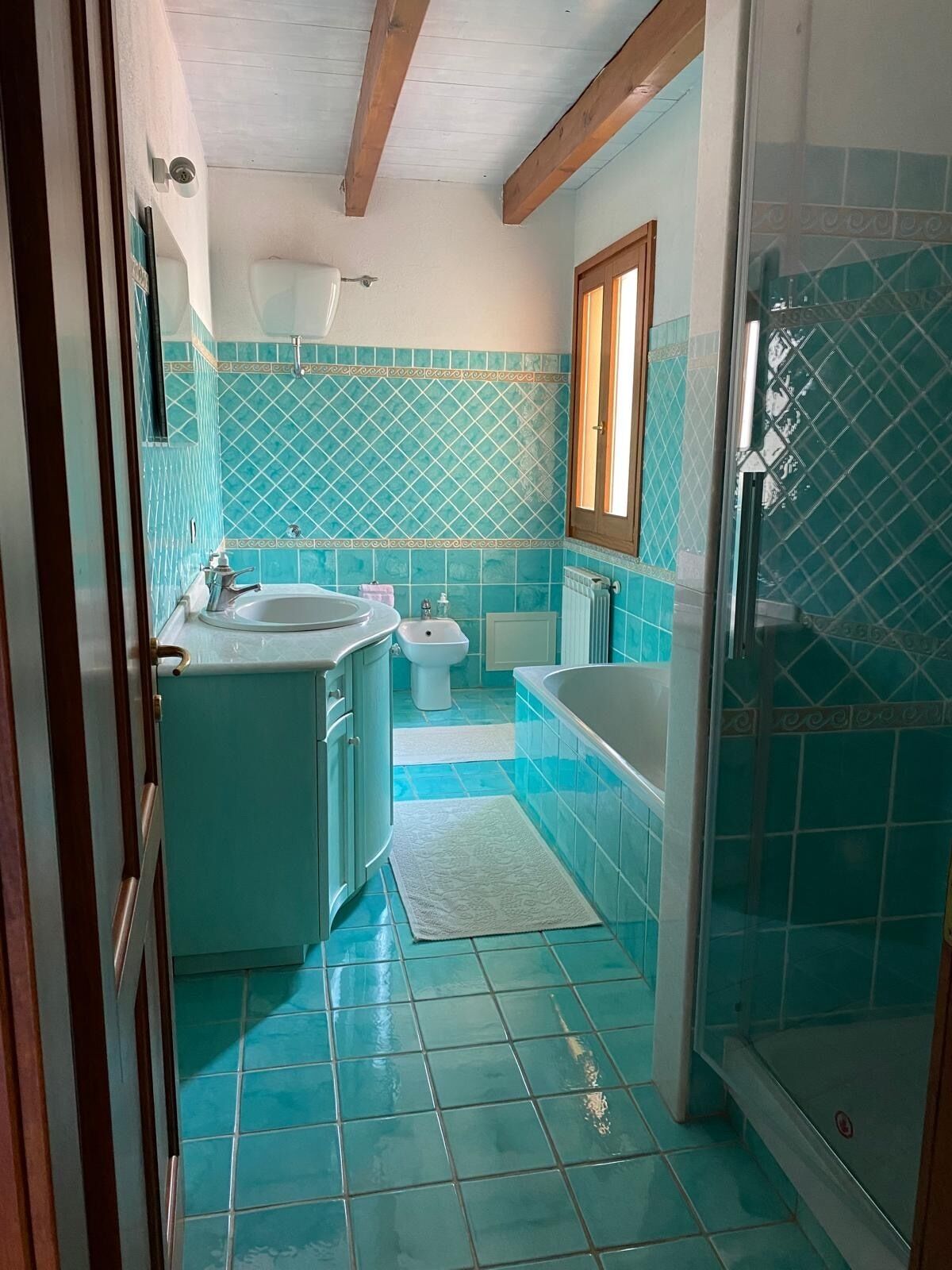 A bathroom with a sink, toilet, and bathtub, featuring blue tiles and wooden beams on the ceiling.