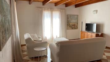 Uma sala de estar com sofá, uma poltrona, uma mesinha, televisão e um quadro na parede.