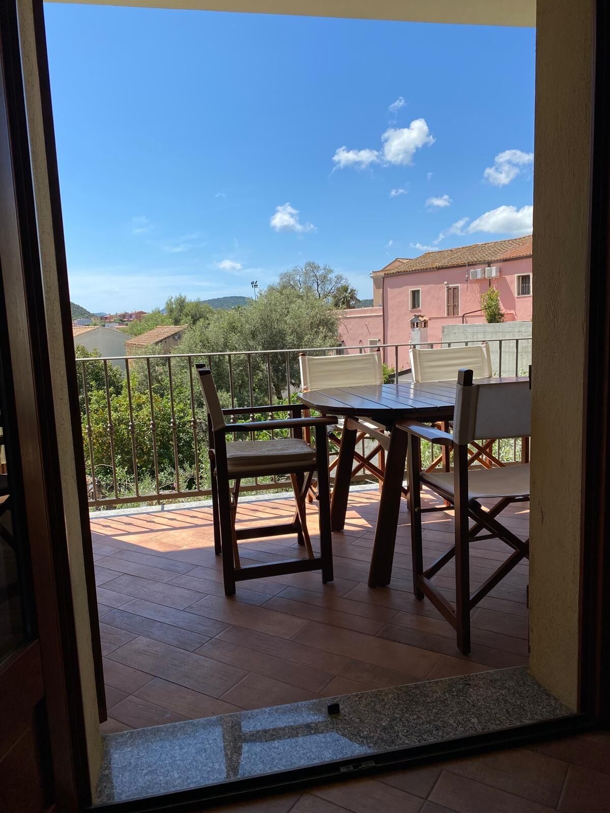 A balcony with a table and chairs, a tiled floor, and a view of buildings and trees.