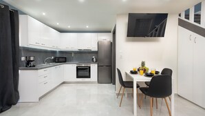 A modern kitchen with white cabinets, a stainless steel refrigerator, and a dining area with a table and chairs. - Golden sand 3 (Ialisos)