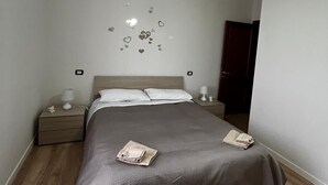 A bedroom with a bed, two bedside tables, a hanging light fixture, and a door in the background. - The Window on Assisi (Bastia Umbra)