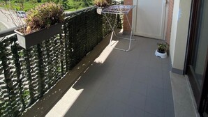 A balcony with a clothes drying rack, a potted plant, and a view of a residential area with houses and trees. - The Window on Assisi (Bastia Umbra)