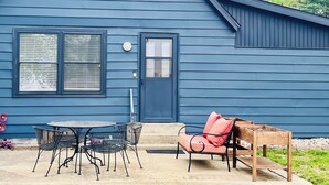A blue house with a front door, two windows, and a patio with a table and chairs. - Charming home on the lake! (Macy)