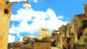 An ancient stone building with a tower, surrounded by ruins and a clear sky. - Central Domus (Matera)