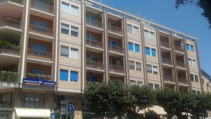 A multi-story building with balconies, a sign for 'Assicurazioni Avanti Investimenti', and a pedestrian crossing sign. - Central Domus (Matera)