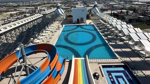 A pool area with a slide and a rainbow-colored lane, surrounded by sun loungers and umbrellas. - Simurg Luxury Halal Hotel (Alanya)