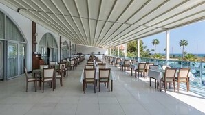 A spacious outdoor dining area with tables and chairs, large windows, and a view of the ocean. - Simurg Luxury Halal Hotel (Alanya)