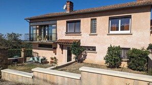Une maison à deux étages dotée d’un balcon, d’une terrasse avec des meubles d’extérieur et d’un petit jardin.