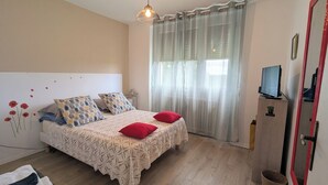 Une chambre à coucher avec un lit, deux oreillers, une télévision et une fenêtre avec des rideaux.
