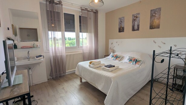 Une chambre à coucher comprenant un lit, une table de chevet, une fenêtre avec des rideaux, un radiateur et des œuvres d’art murales.