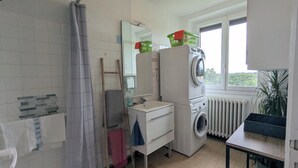 Une salle de bain équipée d’un lave-linge, d’un lavabo, d’un miroir et d’une fenêtre.
