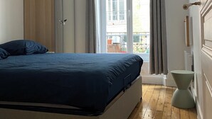 A bedroom with a bed, wooden wardrobe, ceiling fan, and a window with curtains.