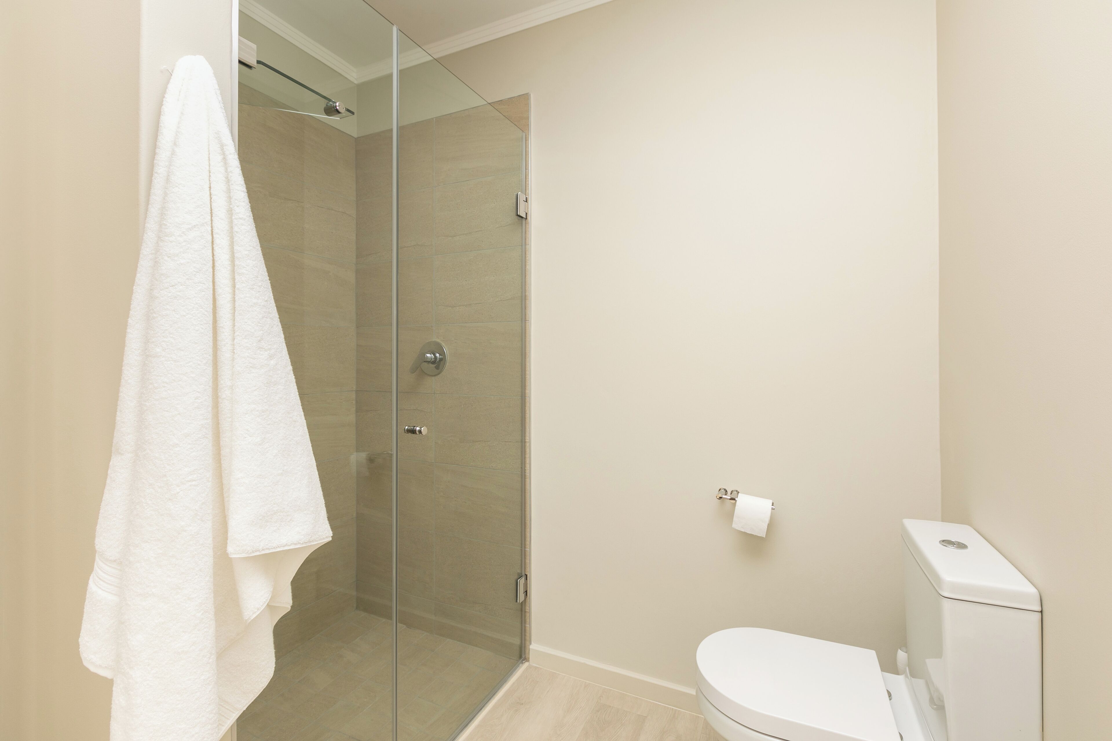A bathroom with a glass shower enclosure, a toilet, and a towel hanging on the wall.