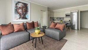 Ein modernes Wohnzimmer mit einer grauen Eckcouch, einem runden Couchtisch und einem großen Gemälde an der Wand.