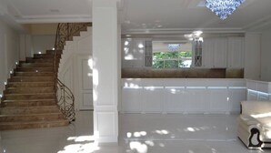 A spacious living area with a staircase, a chandelier, and a view of greenery outside. - Adams Hotel (Yerevan)