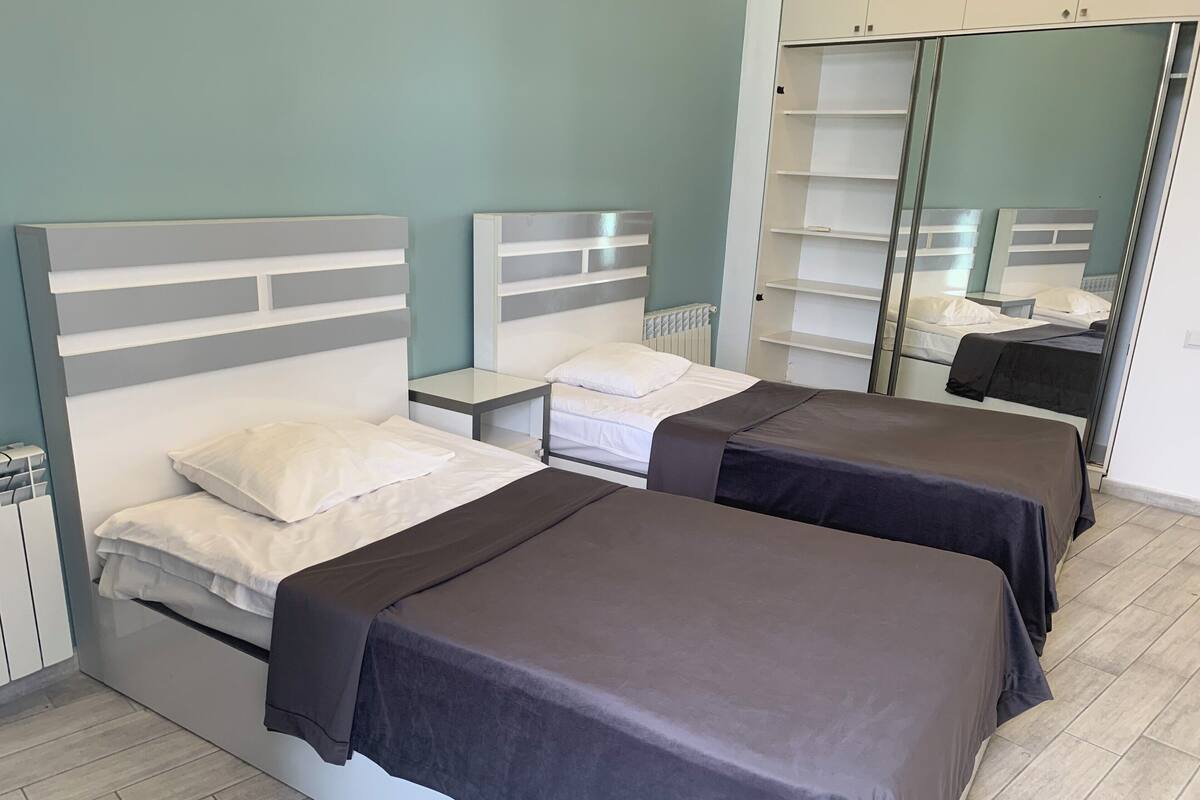 A hotel room with two beds, a wardrobe, a bedside table, and a mirror.
