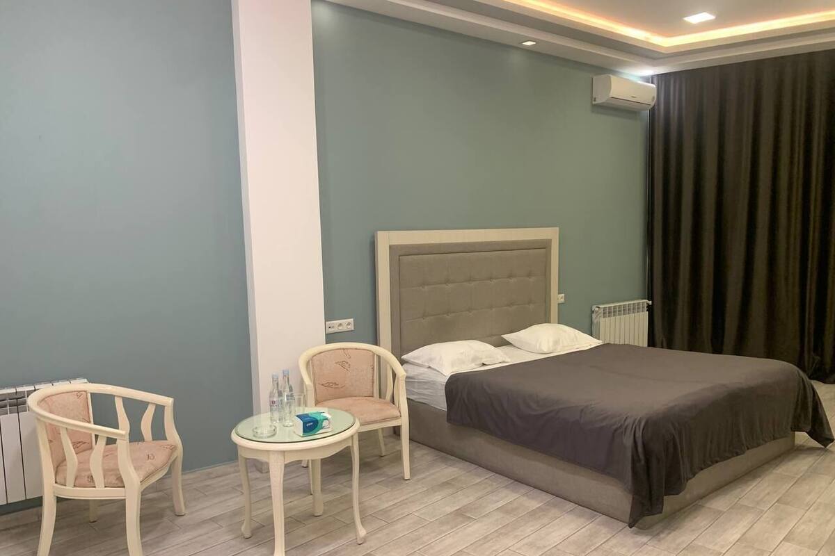 A hotel room with a bed, two chairs, a small table, and a radiator.