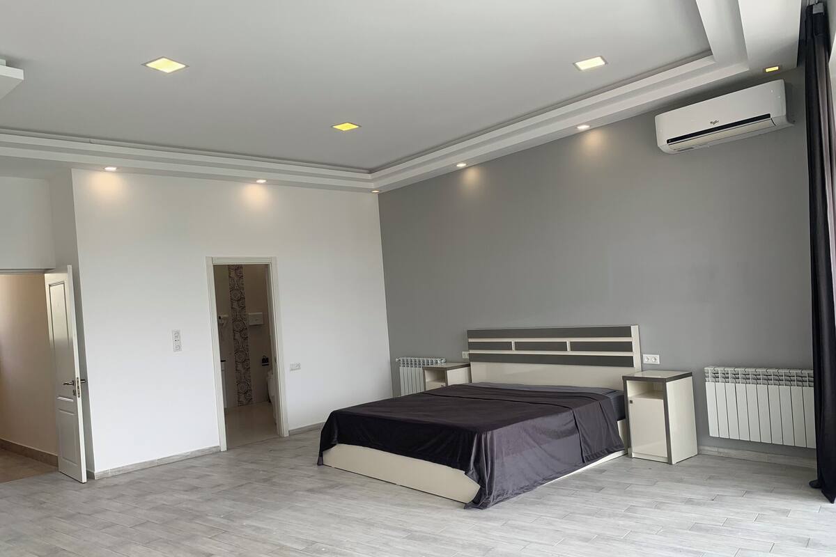 A modern bedroom with a bed, bedside tables, an air conditioning unit, and a radiator.