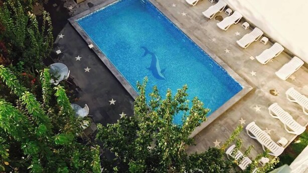 A rectangular swimming pool with a clear blue water surface, surrounded by white lounge chairs and a few small white tables. - Adams Hotel (Yerevan)