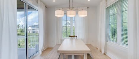 Un vaste espace dédié à la salle à manger, avec une longue table et des bancs, de grandes fenêtres équipées de stores et un luminaire au plafond.