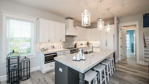 A modern kitchen with white cabinetry, a marble island, pendant lighting, and a view to the outdoors. - Surfer's Dream- 4 bedroom close to beach, pool and spa with rooftop (Holmes Beach)
