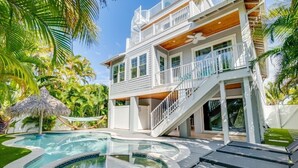 A two-story house with a swimming pool, a wooden deck, and a staircase leading to the upper level. - Surfer's Dream- 4 bedroom close to beach, pool and spa with rooftop (Holmes Beach)
