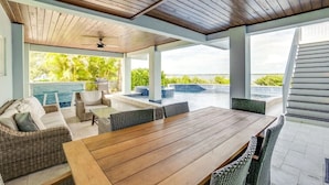A covered outdoor area with a wooden ceiling, a pool, wicker furniture, and a view of the ocean.