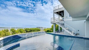 A swimming pool with a clear view of the water, a covered area with stairs, and a view of the surrounding greenery and distant land.