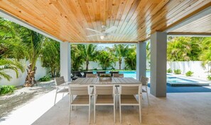 A covered outdoor dining area with a wooden ceiling, a pool, and palm trees. - Anna Maria Beach House- 5 bedrooms close to beach- Private pool and spa (Anna Maria)