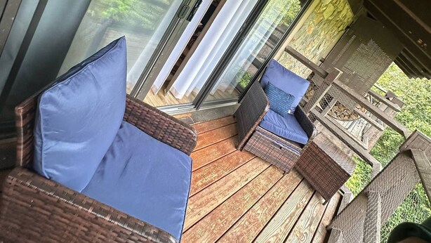 A covered outdoor seating area with wicker furniture and blue cushions, overlooking a lush green landscape. - Charming 1-bedroom, one-loft condo in beautiful Sevierville, with pool and WiFi. (Sevierville)