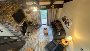 A spacious living area with a stone fireplace, a sofa set, a coffee table, and a staircase leading to an upper level. - Charming 1-bedroom, one-loft condo in beautiful Sevierville, with pool and WiFi. (Sevierville)