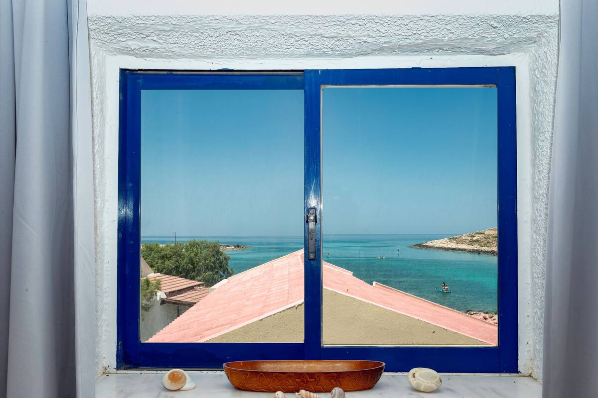 A window with a blue frame and a view of a beach with buildings in the background.