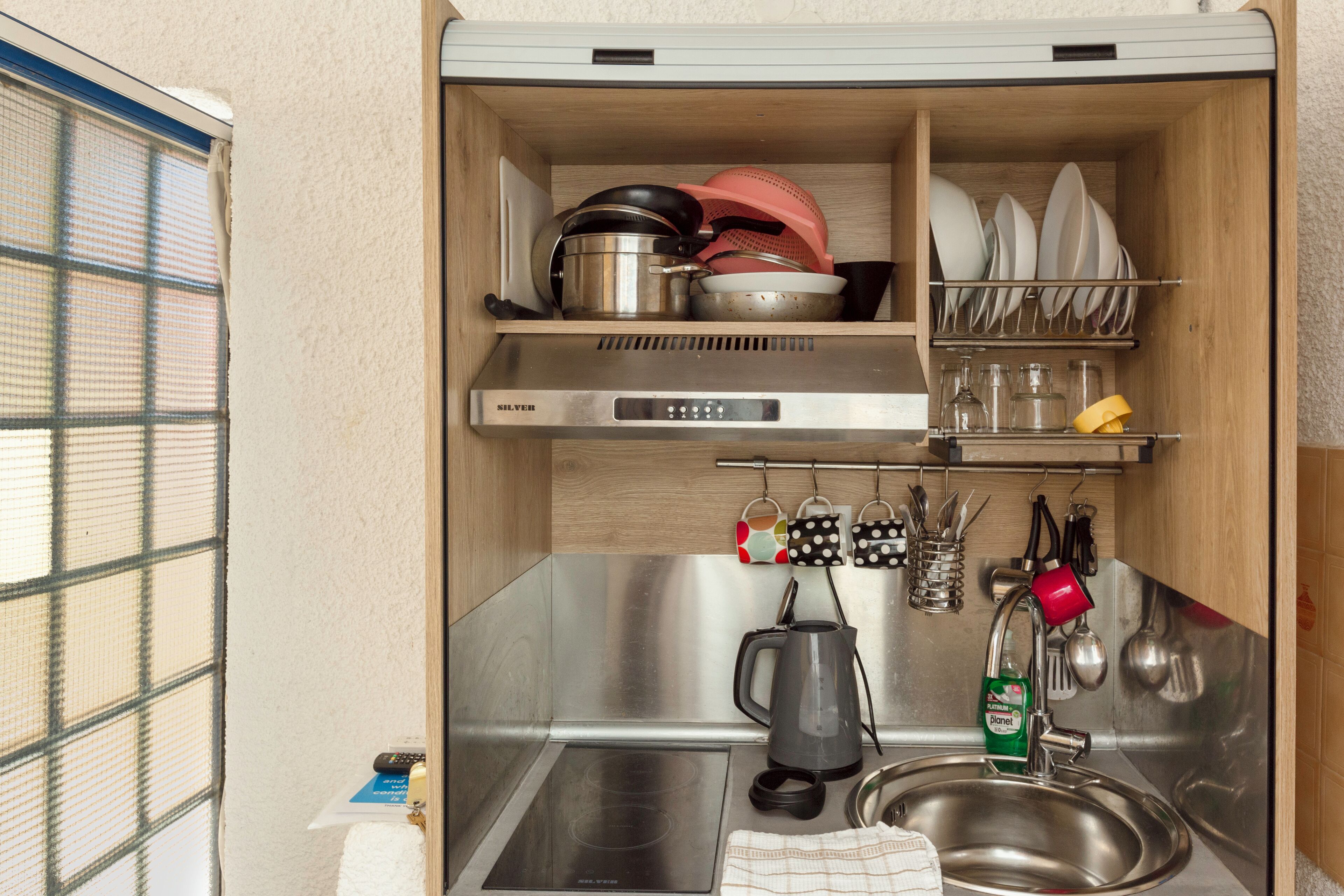 A compact kitchen with a built-in stove, a sink, and shelves above for dishes and cookware.