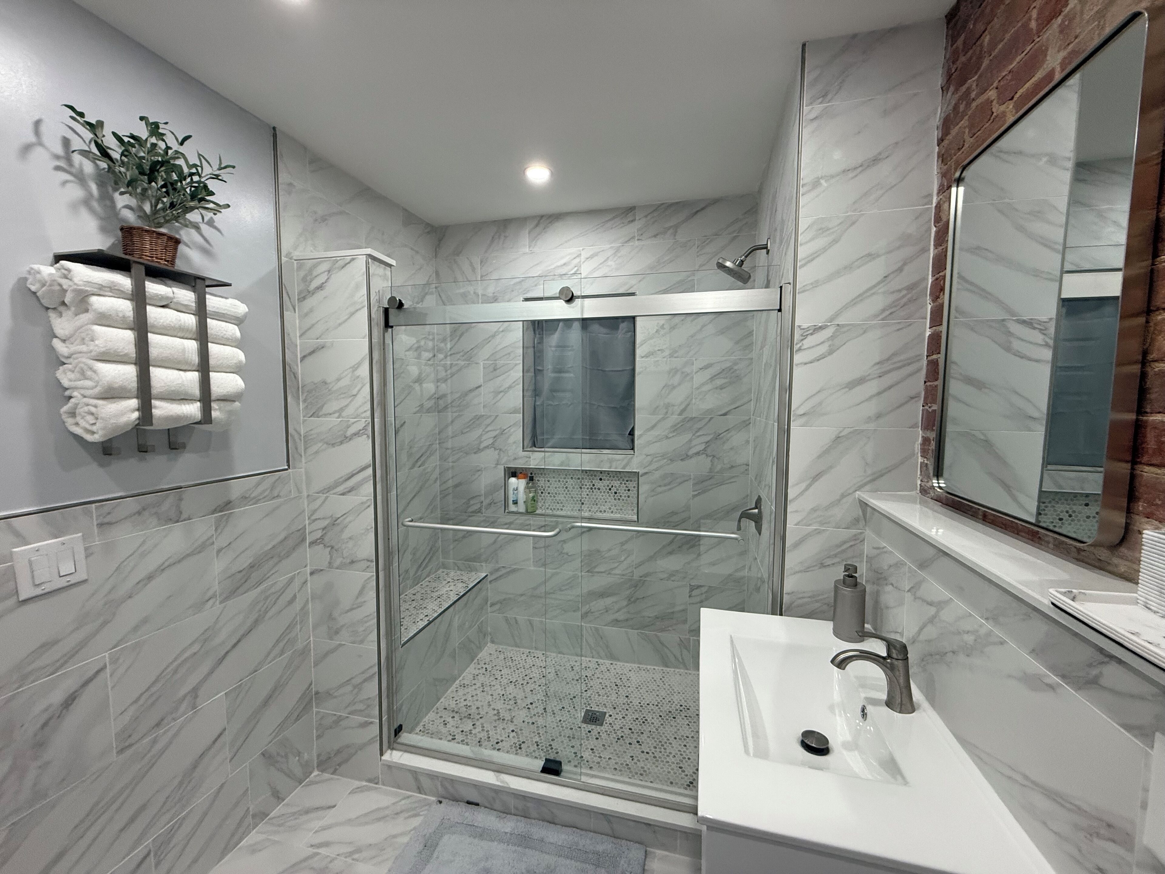 A modern bathroom with a glass-enclosed shower, a white sink, and a large mirror.