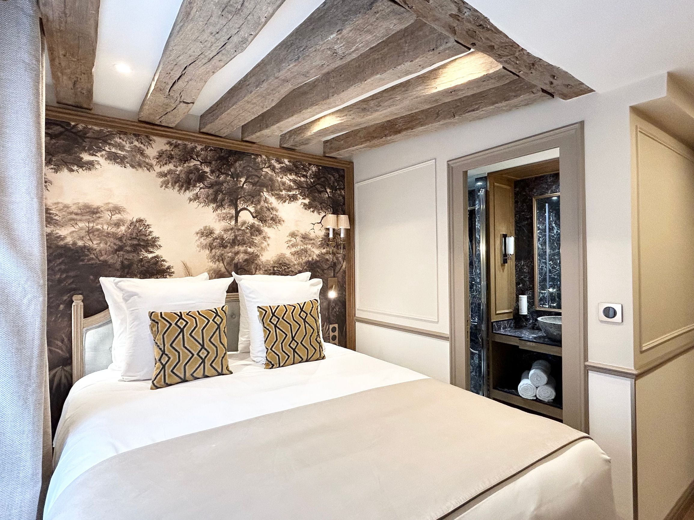 A bedroom with a bed, a wall-mounted mirror, and a wooden ceiling.