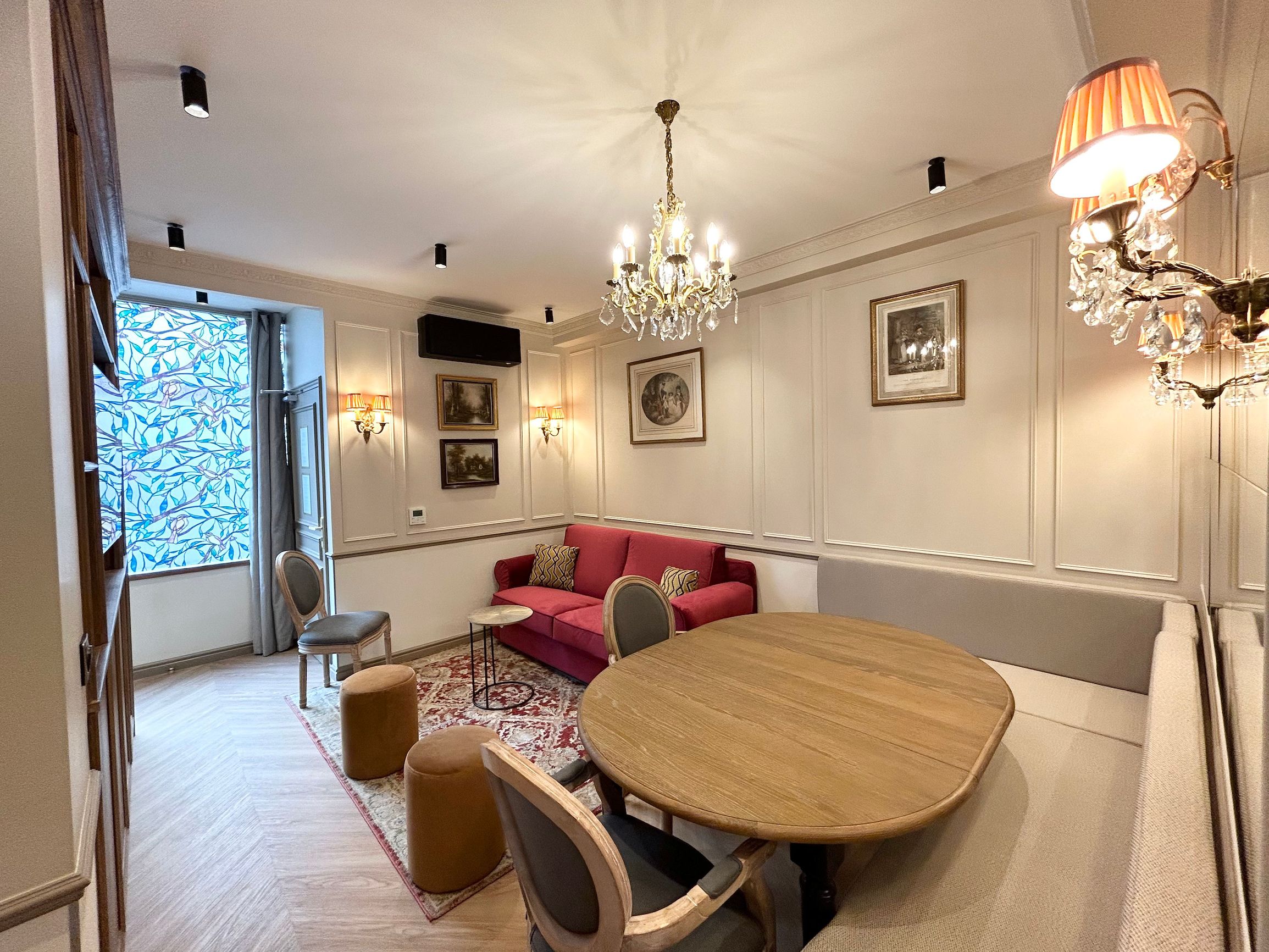 A dining area with a wooden table and chairs, a red sofa, and a chandelier.