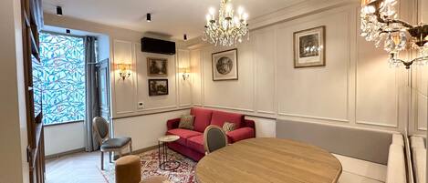 A dining area with a wooden table and chairs, a red sofa, and a chandelier.