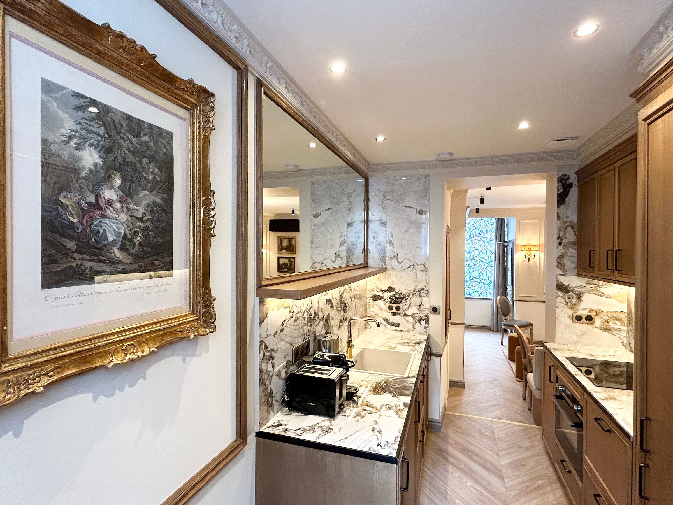 A modern kitchen with marble countertops, a sink, and a toaster. There is a framed artwork on the wall and a mirror above the sink.