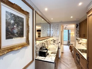A modern kitchen with marble countertops, a sink, and a toaster. There is a framed artwork on the wall and a mirror above the sink. - Merveil - Signature Suite - Tour Eiffel - Bourgogne (Paris)