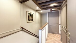 A staircase with wooden handrails and a herringbone-patterned floor leading to a door with a brass handle. - Merveil - Signature Suite - Tour Eiffel - Bourgogne (Paris)